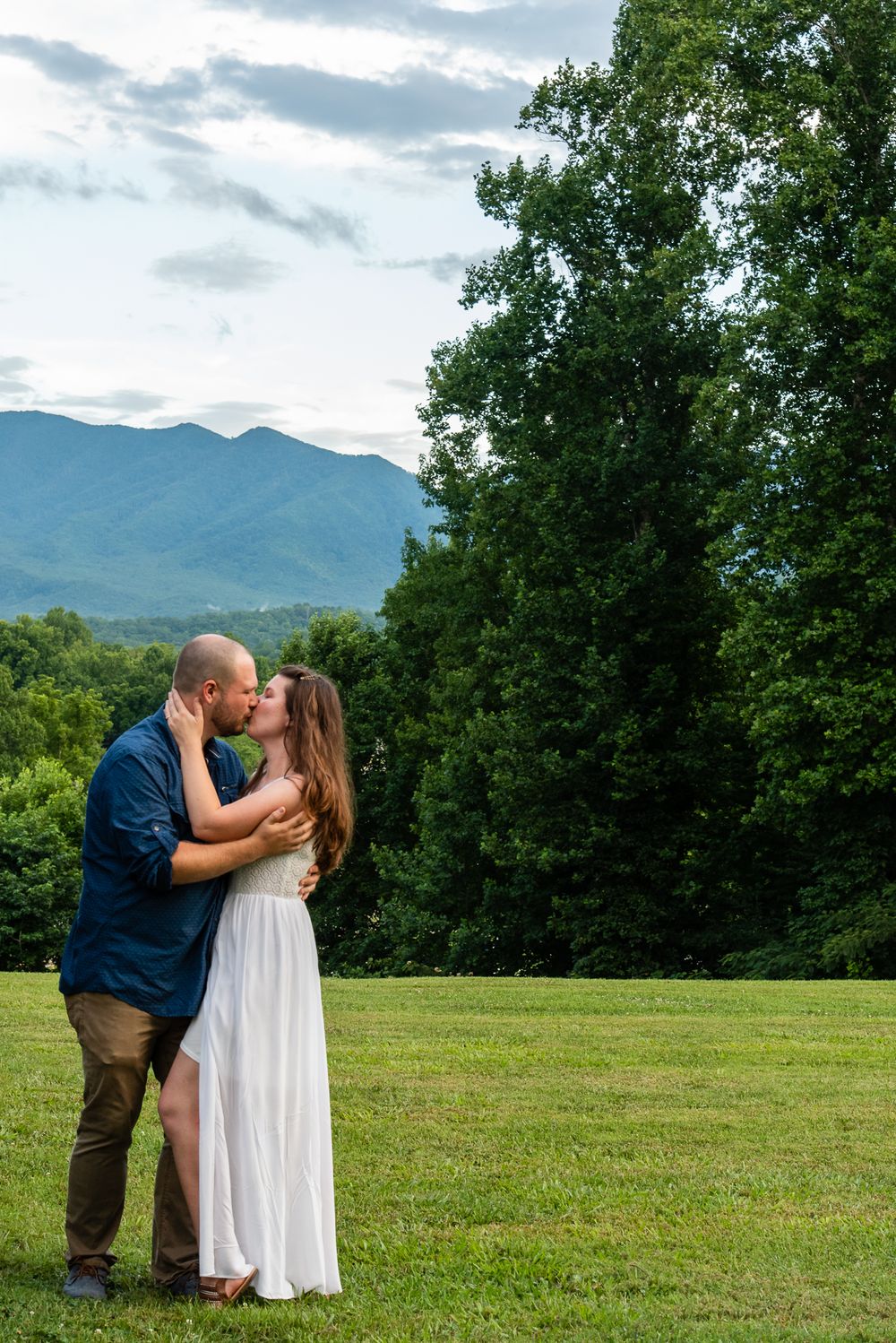 Husband kisses wife passionately with mountains in the background.