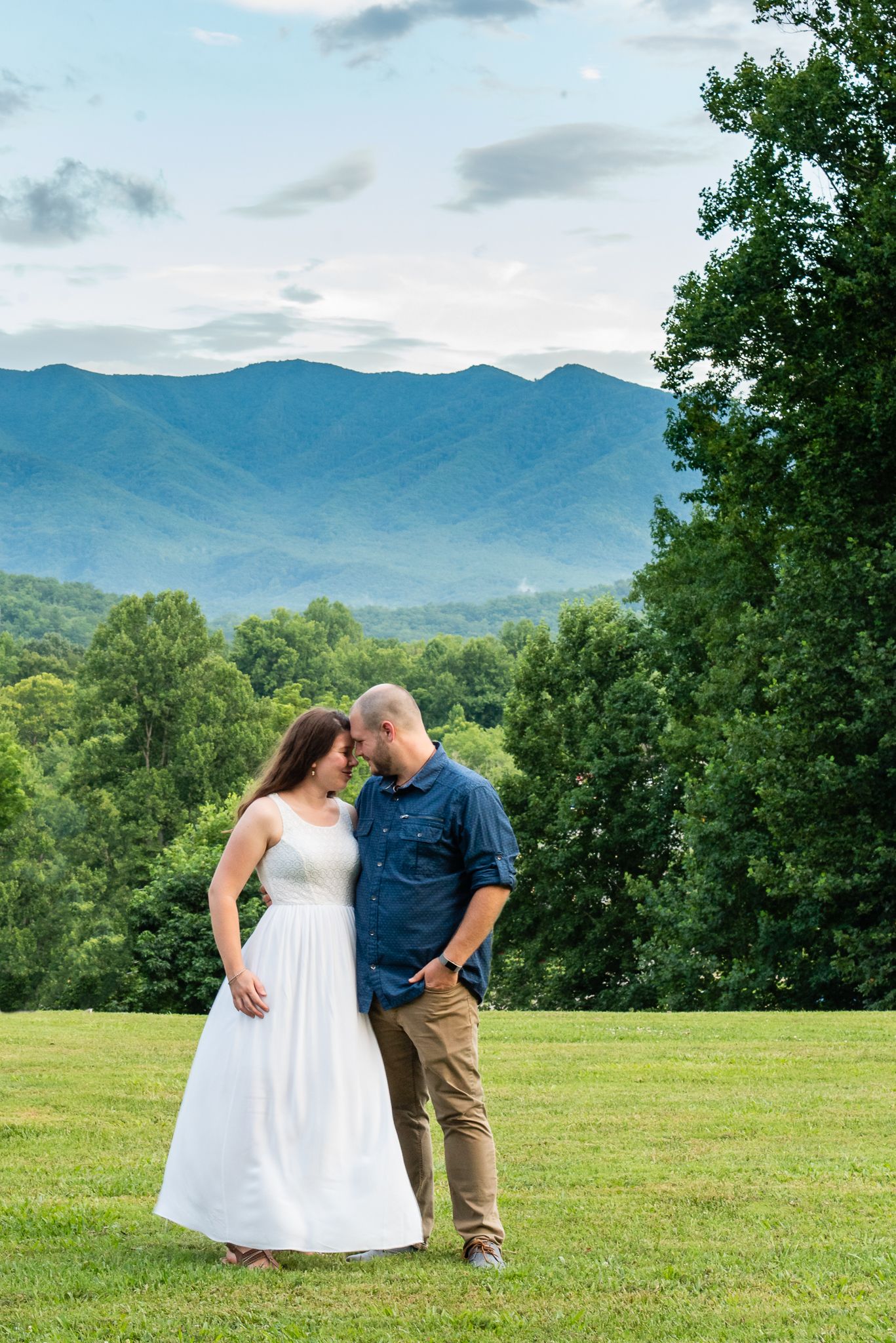 Couple looks windswept with foreheads touching with mountains.