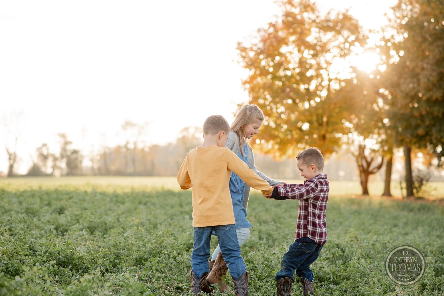 Three people playing and running together in a sunlit field at sunset.