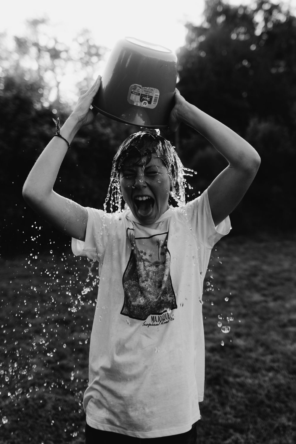 Black and white photo of someone pouring water over themselves outdoors while laughing.