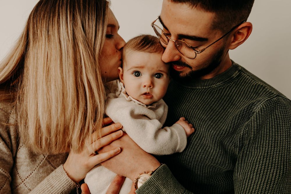 Intimate family moment as parents kiss their baby from both sides.