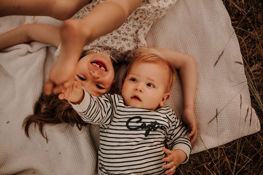 Two children laying on a blanket share playful laughter together outdoors.