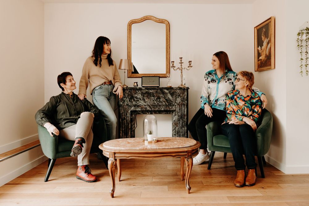 Four people lounging in a vintage-style living room with a white fireplace and decorative mirror.