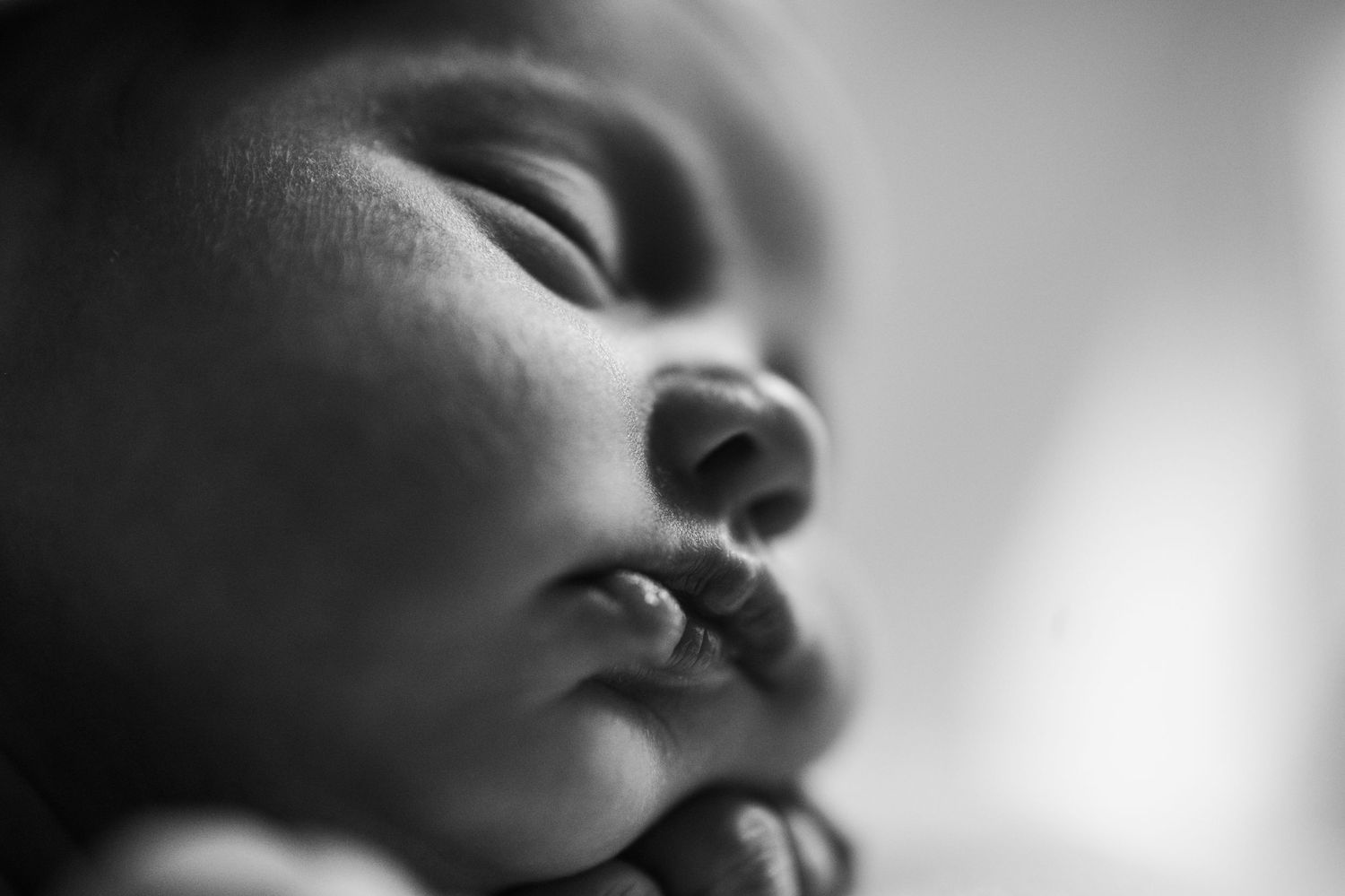 Black and white macro image of a newborn baby's face, focusing on the cheeks and lips in the light