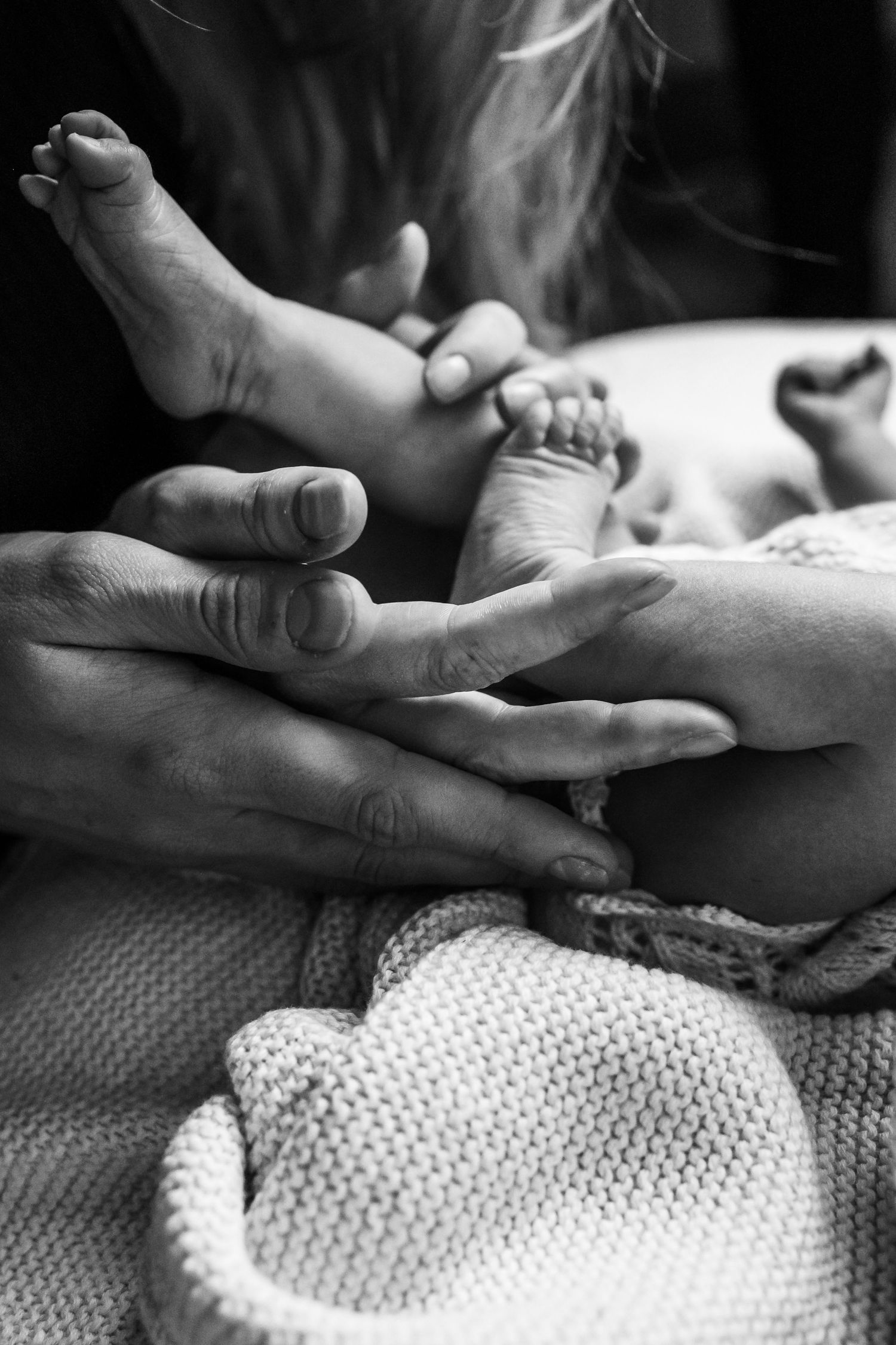 Close up black and white image of a newborn baby's feet enclosed in their parents hands.