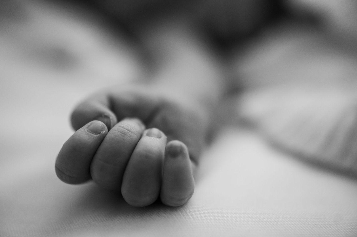 Black and white macro image of a newborn baby's hand, focusing on the tiny fingernails