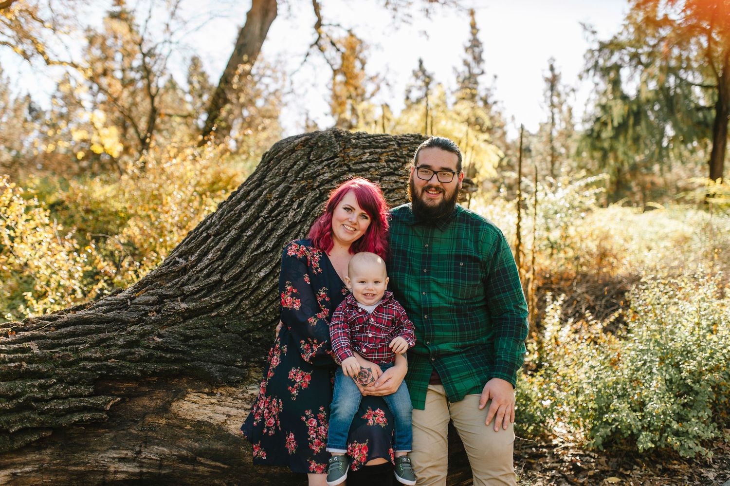 A family poses together on a fallen log surrounded by autumn foliage.