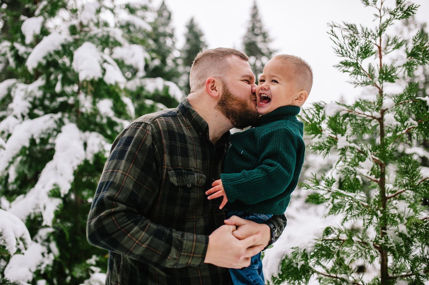 A tender winter moment between two people among snow-covered pine trees.