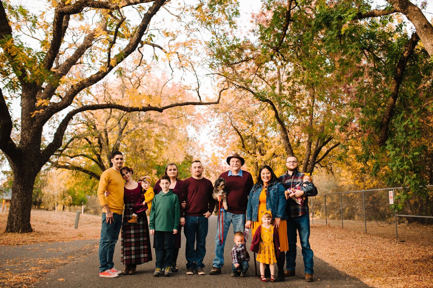 Large group portrait of family members gathered under golden autumn trees.