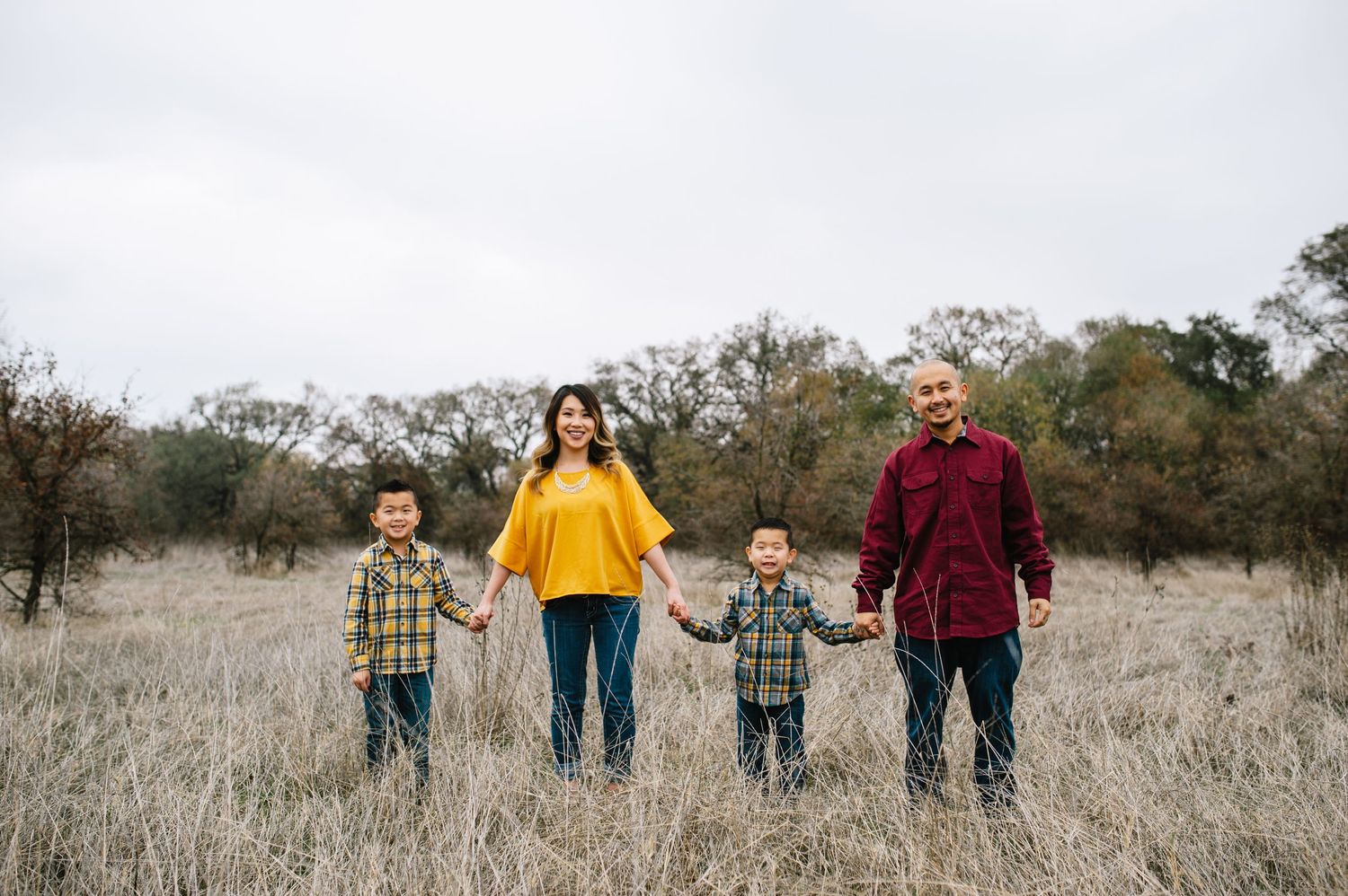 Family of four poses together in a golden field on an overcast day.