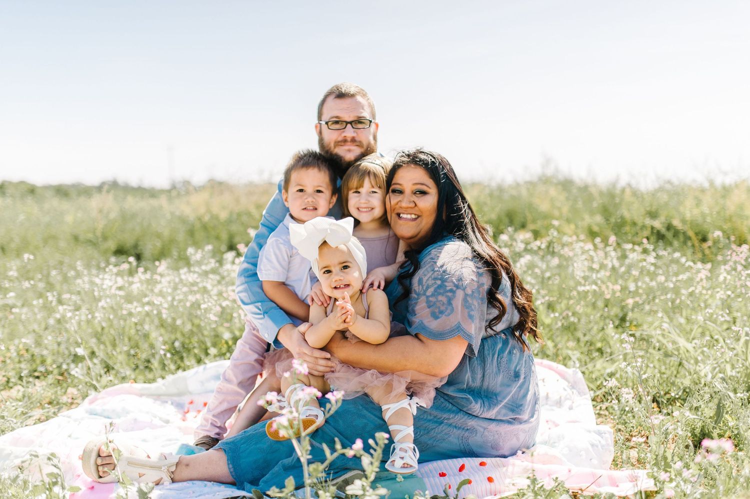 Family enjoying a picnic together in a meadow of white wildflowers on a sunny day.
