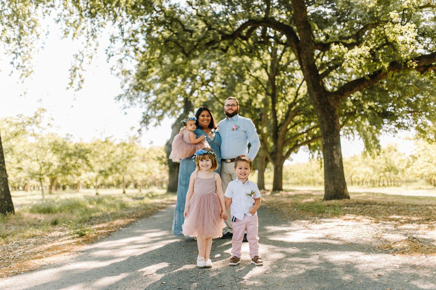 Family portrait on a tree-lined path during golden hour.