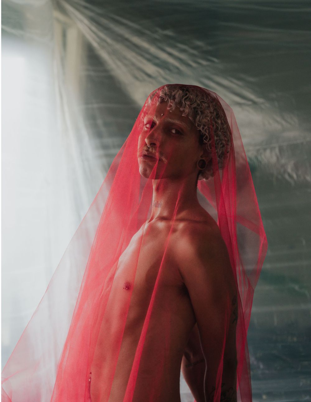 Artistic studio portrait with subject wearing translucent red veil against light backdrop.