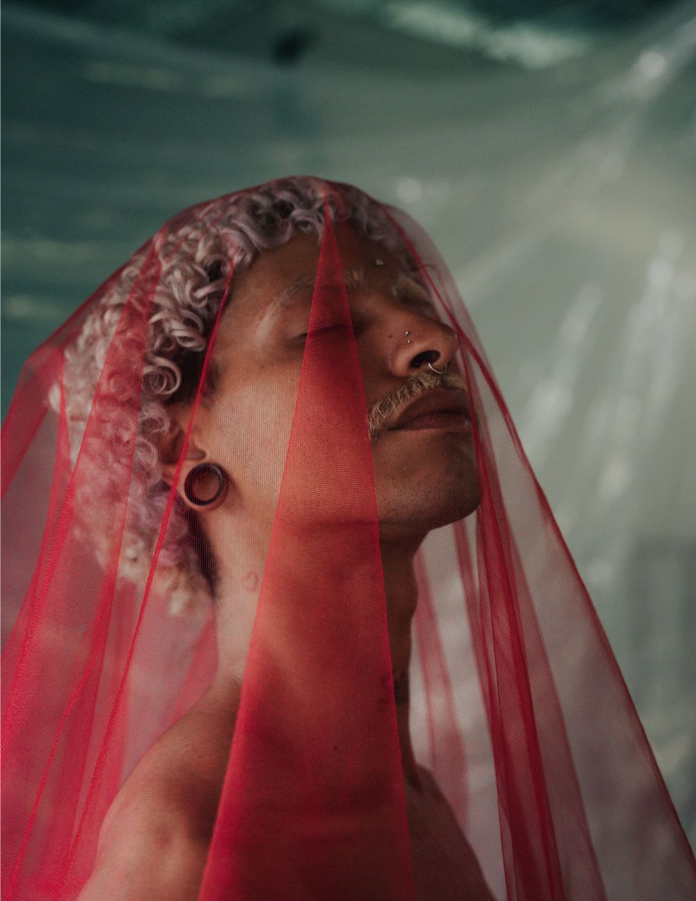 Dramatic close-up portrait with red sheer veil creating ethereal atmosphere.
