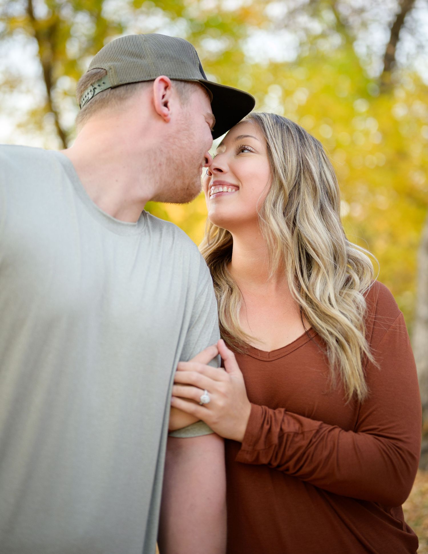 Casual couple sharing intimate moment outdoors with autumn foliage in background.