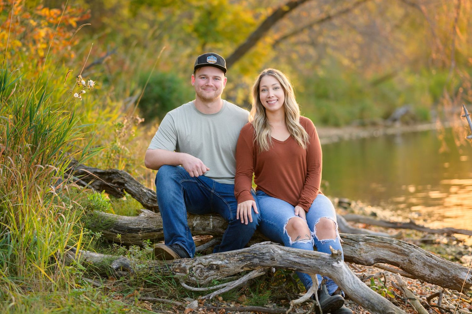 Couple sitting on fallen log by river during autumn photo session.