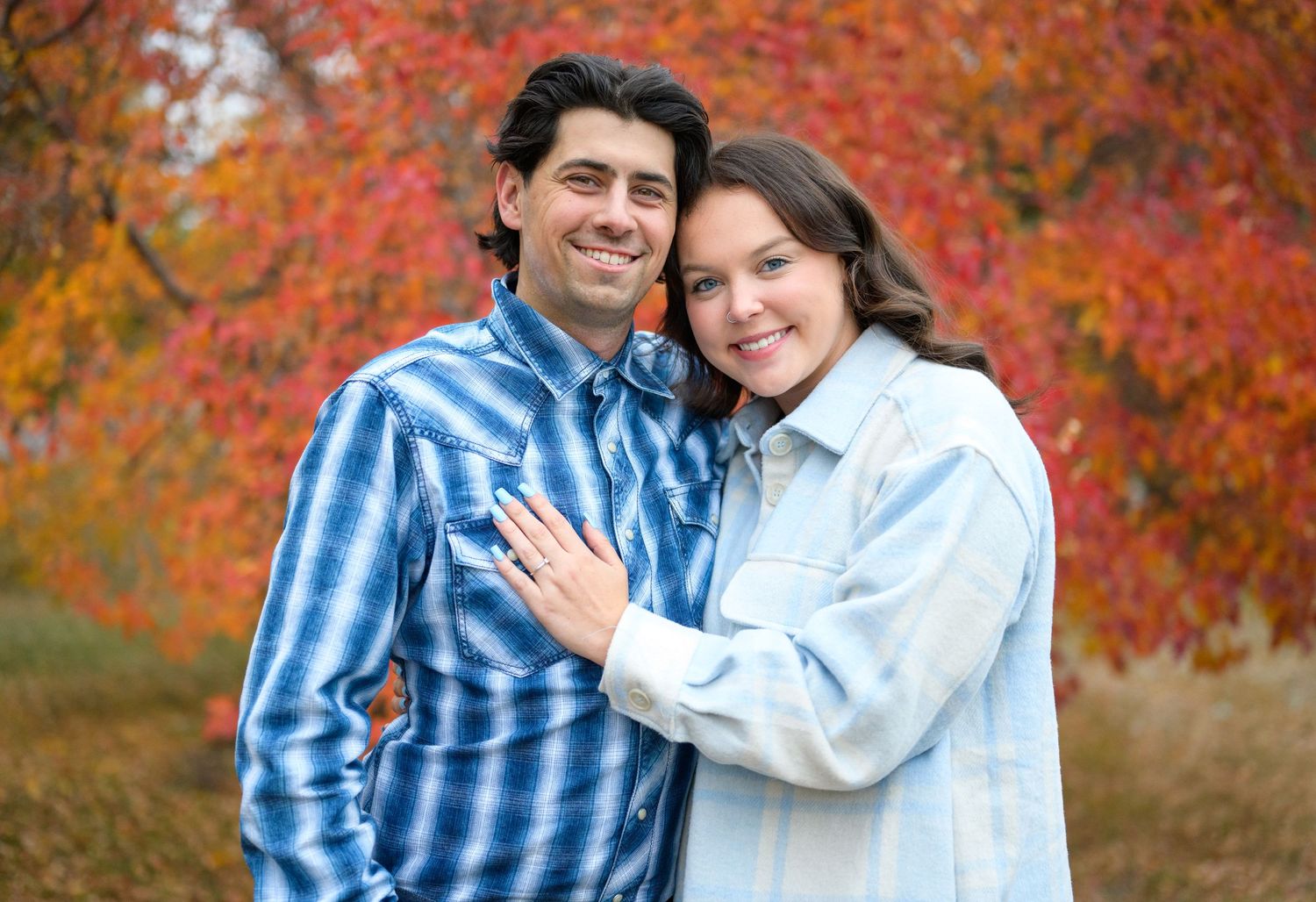 A romantic portrait of a couple posing together against vibrant red fall foliage.