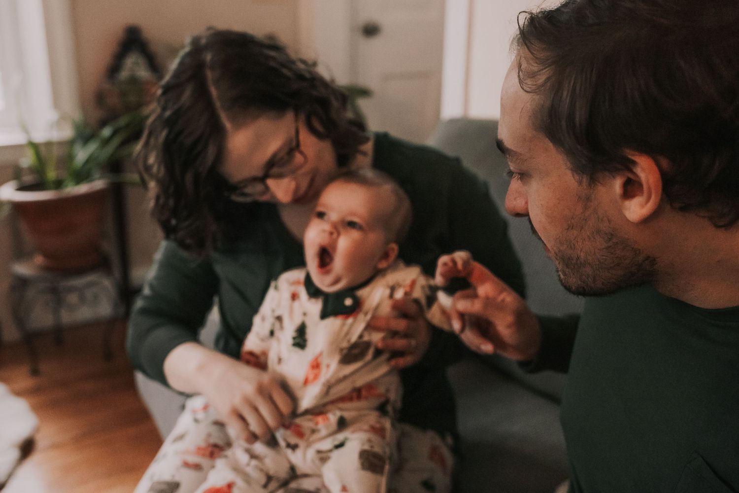 Family members gather together on a couch while feeding and playing with a baby in a warm, cozy home setting at Christmastime in New England