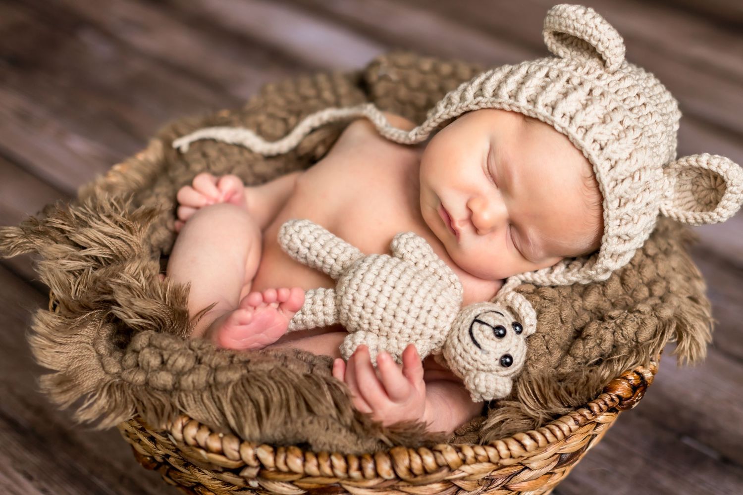 Sleeping newborn in knit hat lying in woven basket on wooden surface.
