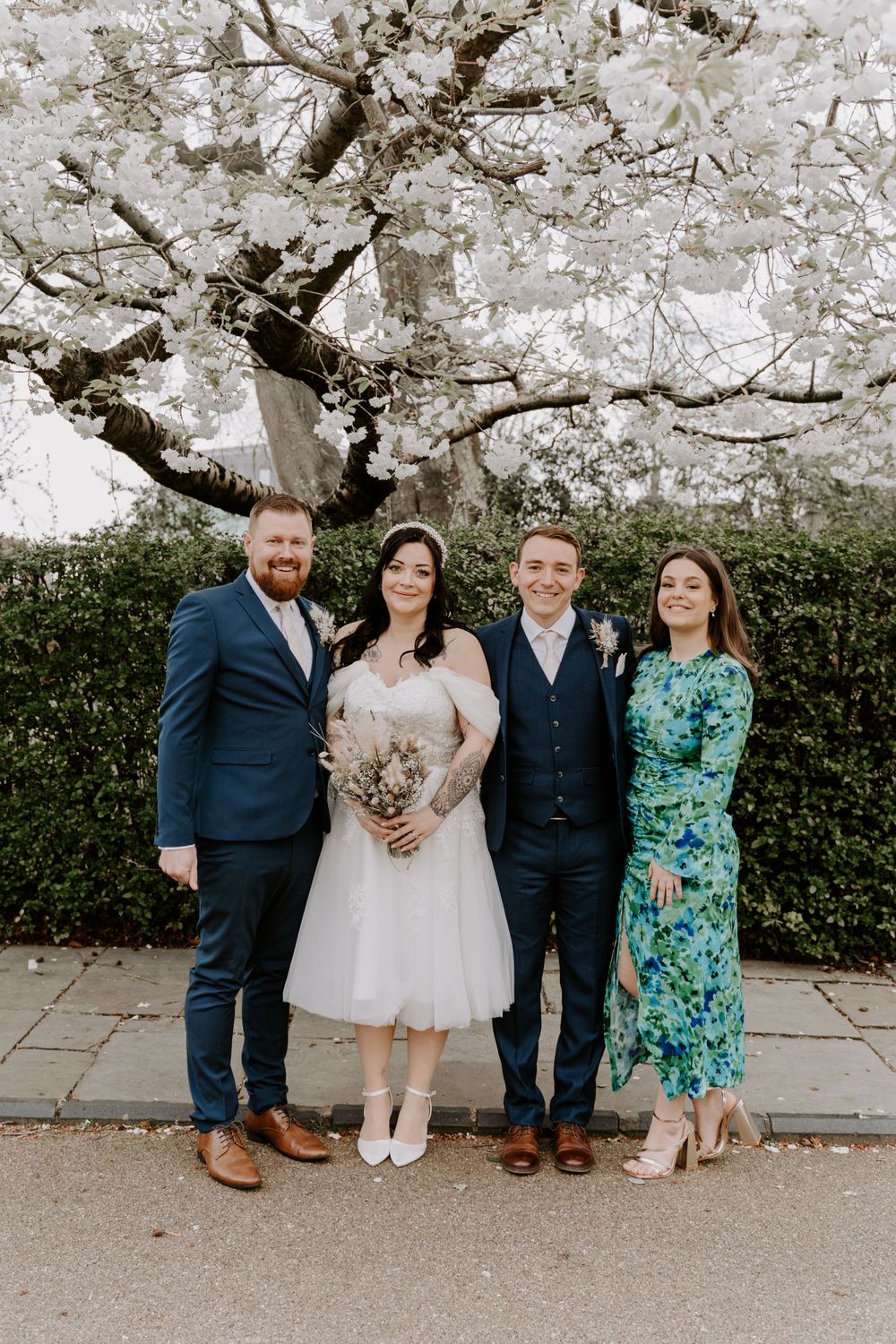 A formal portrait of a bride and groom with two of their wedding guests.