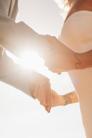 Backlit wedding couple holding hands with visible tattoos and sunburst effect.