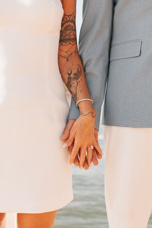 Close-up of intertwined hands showing detailed sleeve tattoos against white and gray formal wear.