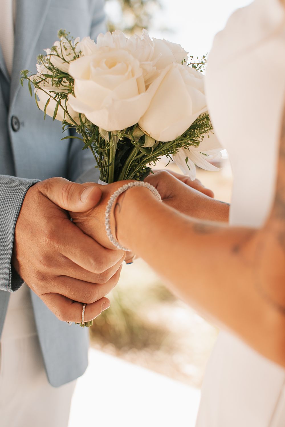 Close-up of hands exchanging white rose bouquet during wedding ceremony.