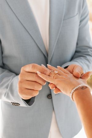 Close-up of hands exchanging wedding rings with light blue suit jacket visible.
