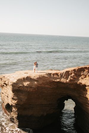 Dramatic coastal cliffside with natural rock arch formation and ocean view at sunset.