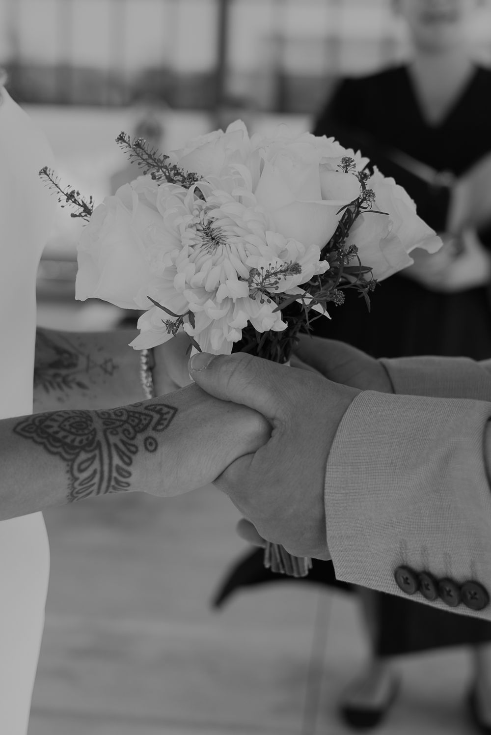 Black and white close-up of hands exchanging wedding flowers during ceremony.
