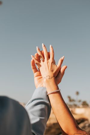 Two hands raised against sky showing matching wave tattoos and bracelets.