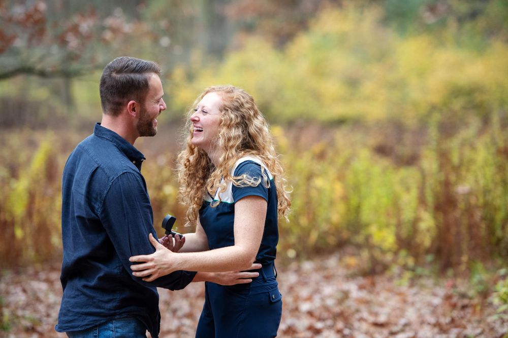 Woman laughing in surprise as her partner proposes with an engagement ring during a fall outdoor proposal