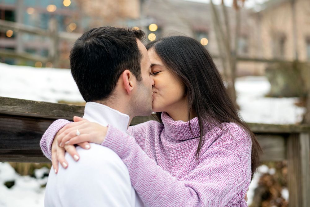 Couple kissing on a wooden bridge during a snowy winter engagement session