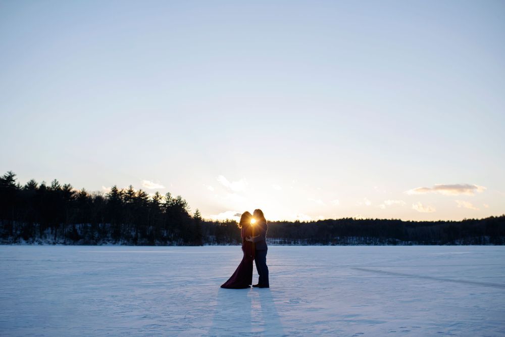Silhouette of an engaged couple embracing at sunset on a frozen lake during a winter engagement session at Walden Pond in Massachusetts
