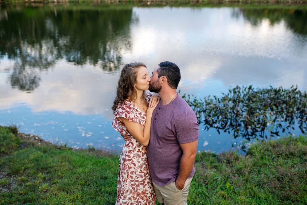 Couple kissing beside a peaceful pond during an outdoor engagement session at