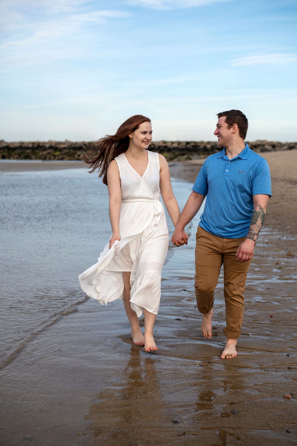 Engaged couple walking barefoot hand in hand along the shoreline during a New England beach engagement session