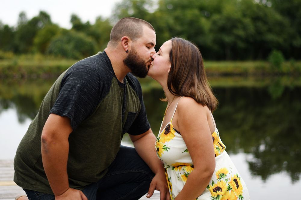 Engaged couple kissing beside a pond during a relaxed outdoor engagement session