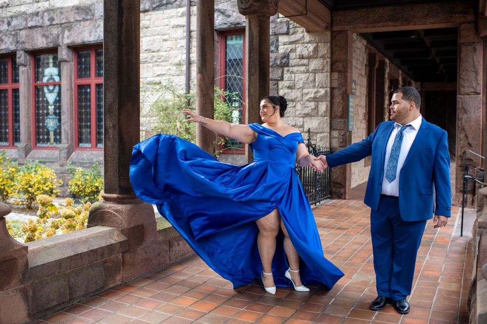Woman twirling in a vibrant blue gown while holding her fiancé's hand during an elegant engagement session  at Trinity Church in Boston