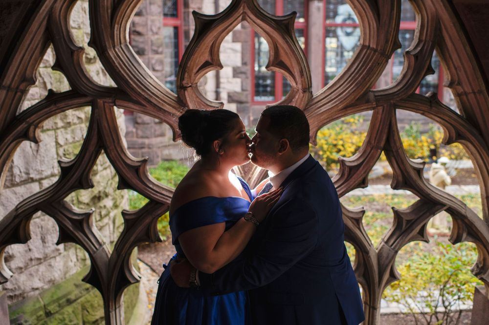 Couple sharing a kiss beneath ornate Gothic stonework during an elegant engagement session at Trinity Church in Copley Square in Boston
