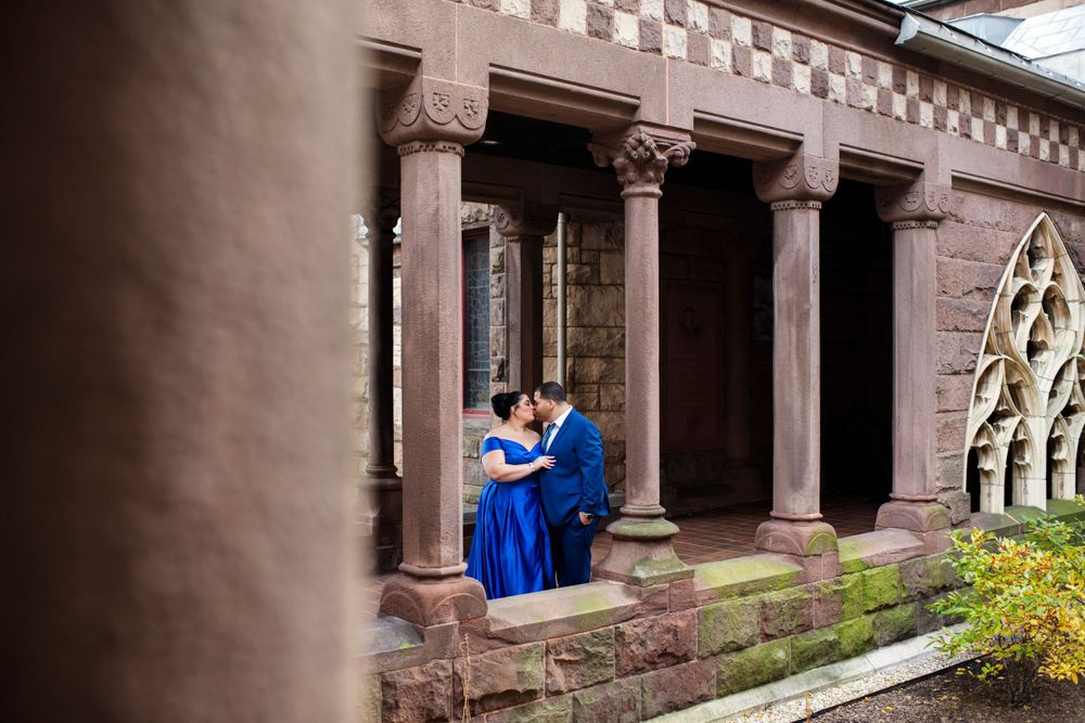 Engaged couple kissing beneath the stone columns of Trinity Church in Copley Square in Boston during their engagement session