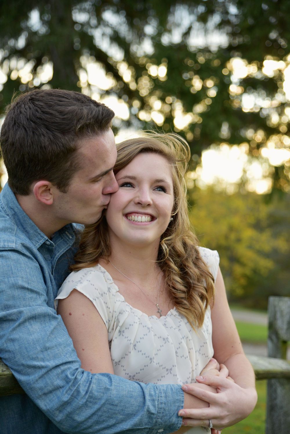 Man kissing his smiling fiancée on the cheek during a golden-hour engagement portrait