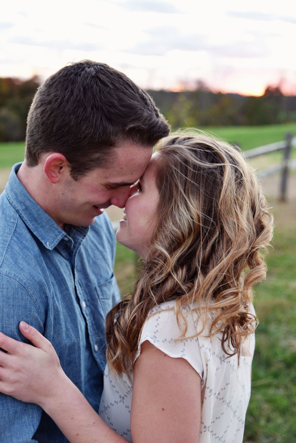 Engaged couple touching foreheads and smiling during a romantic outdoor portrait at sunset
