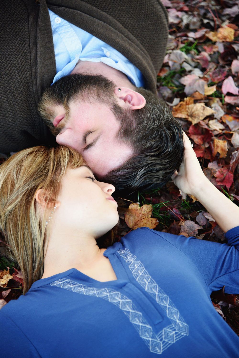Engaged couple lying together among colorful autumn leaves during a fall engagement portrait