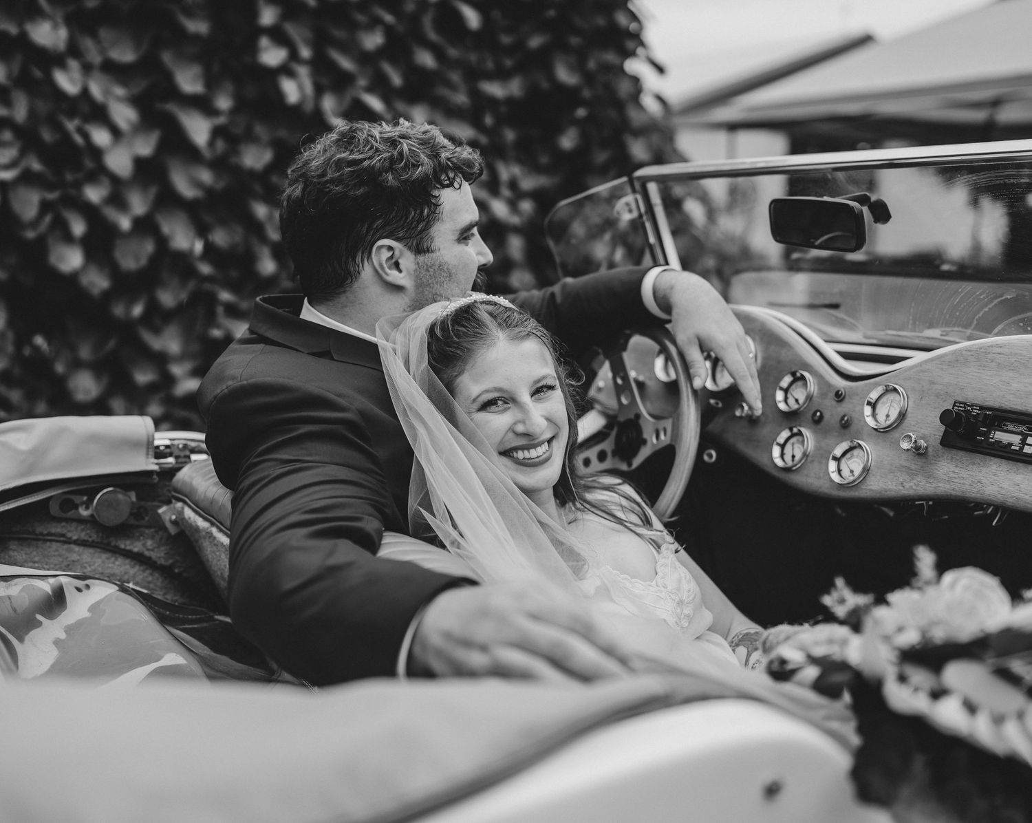Vintage black and white photo of newlyweds enjoying a ride in classic convertible car.