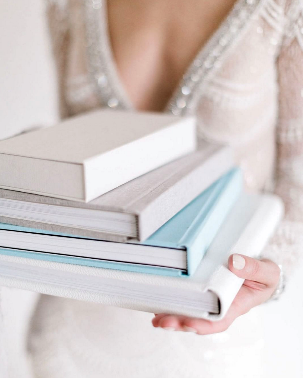A person holding a small stack of minimalist, linen-bound books or wedding albums in neutral tones.