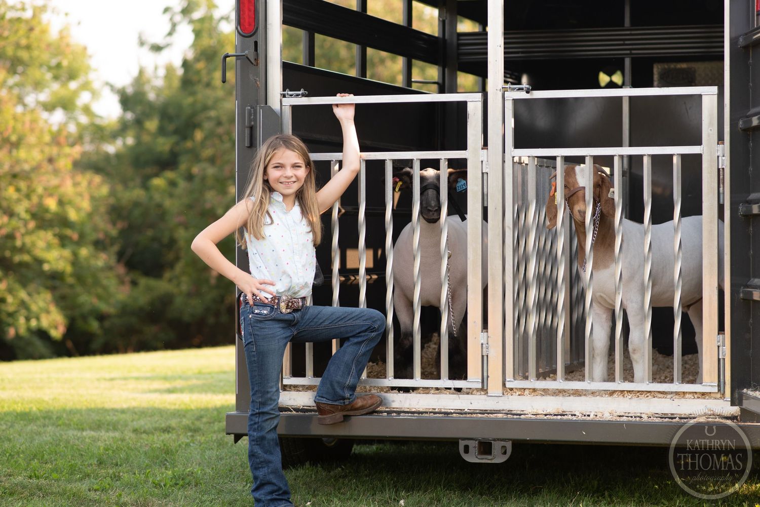 Person stands confidently by a horse trailer in casual western wear.