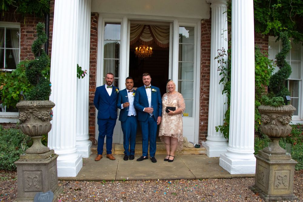 Wedding party poses on grand entrance steps with white columns at elegant brick venue entrance.