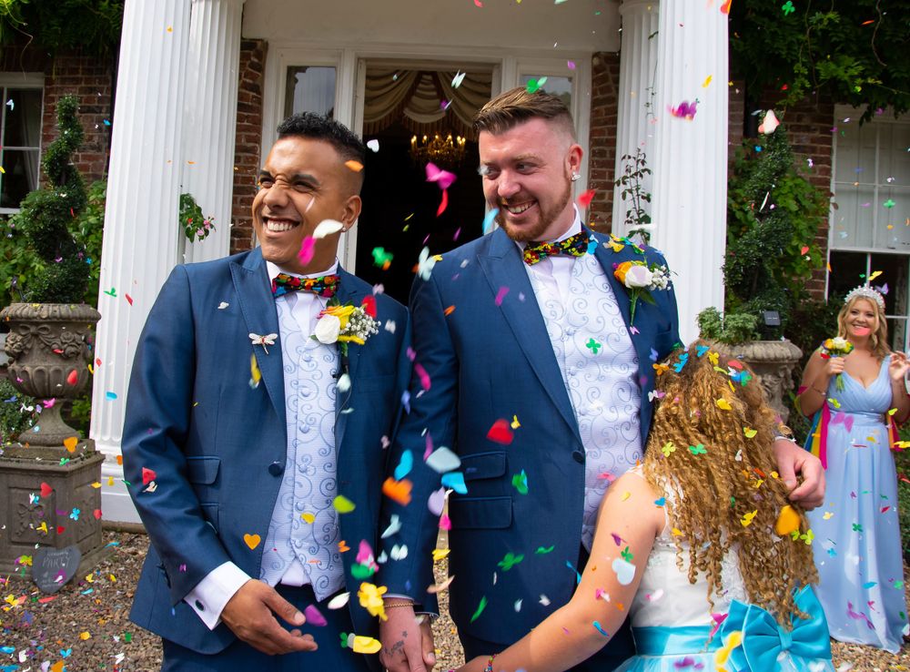 Newlyweds celebrate under white columns as colorful confetti rains down around them.
