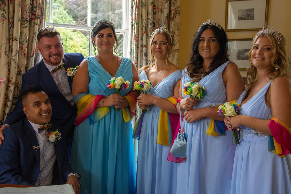 Wedding party in shades of blue and turquoise dresses hold colorful bouquets indoors.