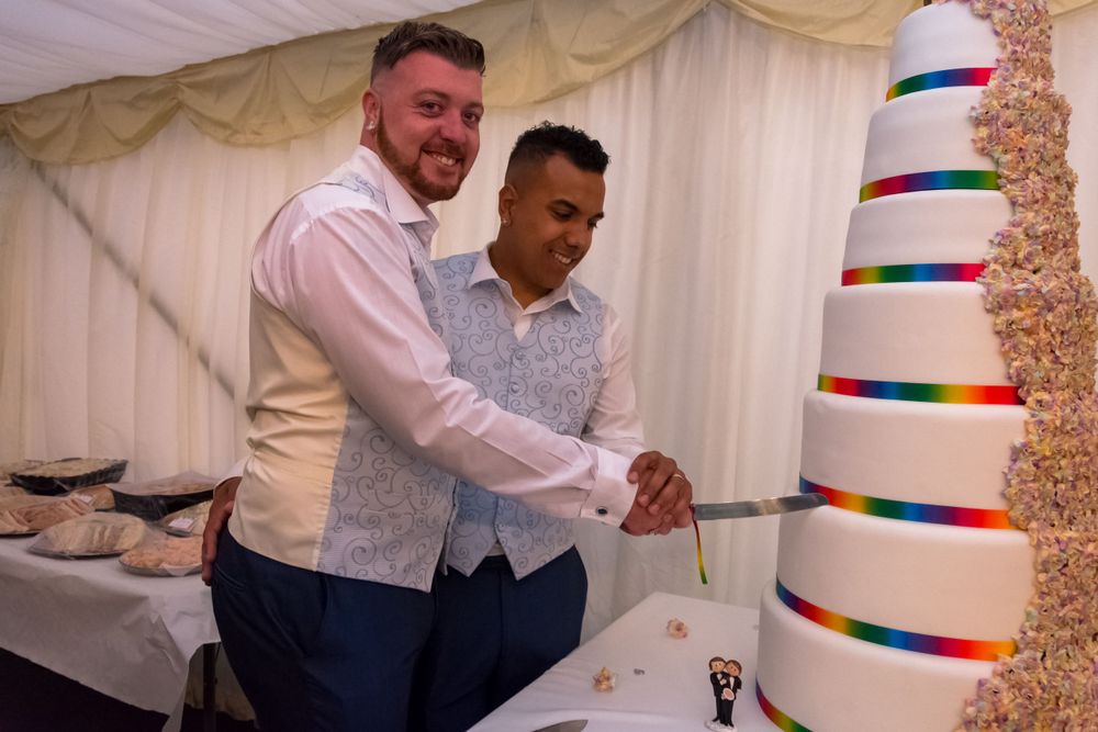 Wedding couple cutting their modern striped rainbow wedding cake in a white reception tent.